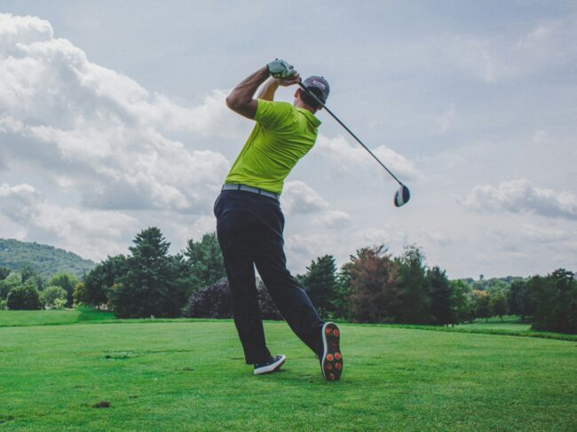 Male golfer in yellow top driving off from a grassy tee on a cloudy day