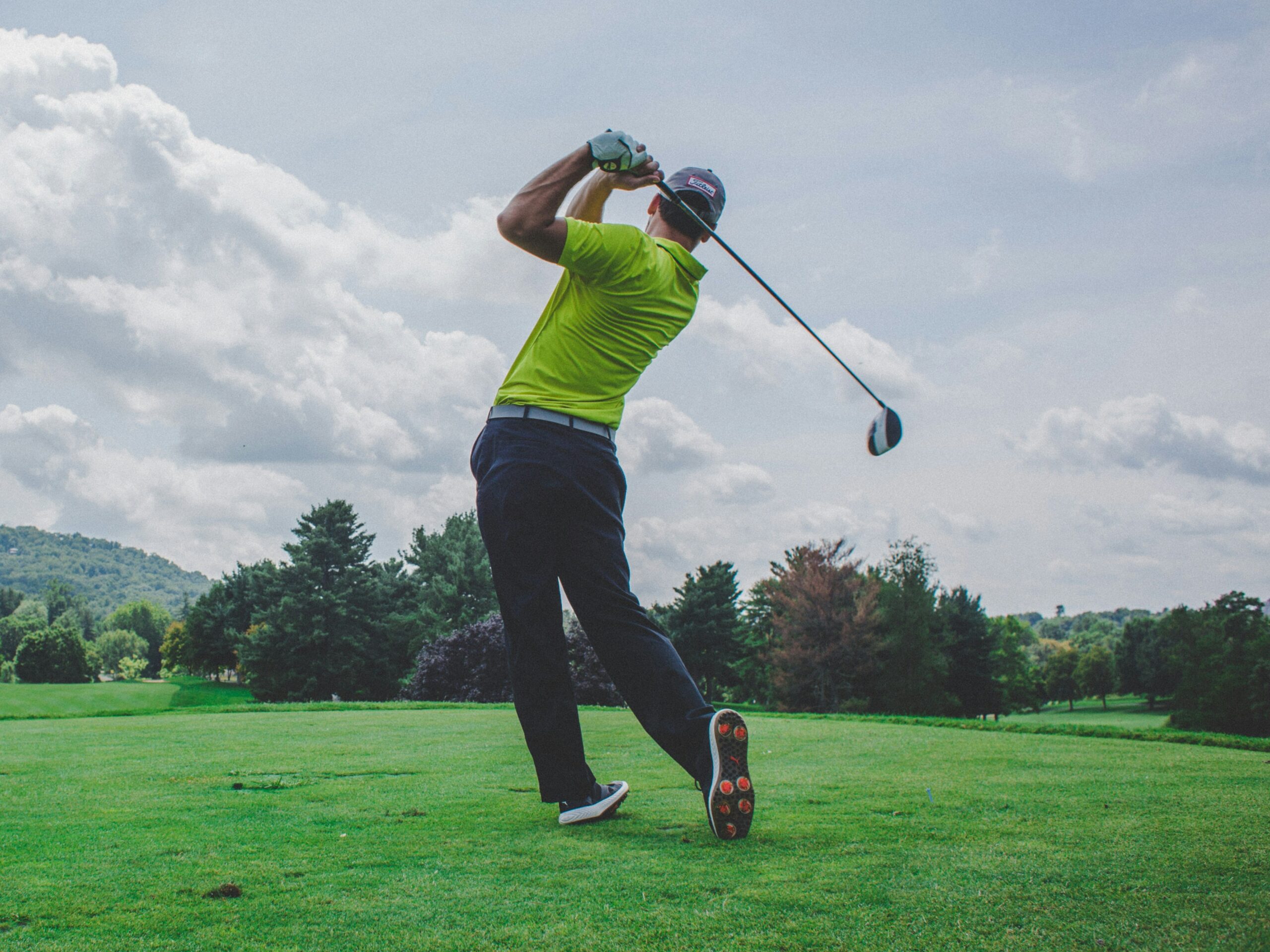 Male golfer in yellow top driving off from a grassy tee on a cloudy day